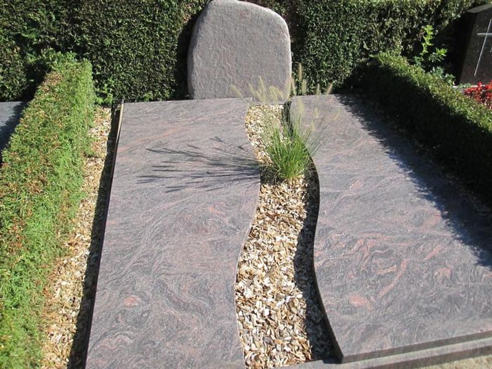 Grabstätte mit Abdeckplatten aus rötlichem Granit und geschwungenem Kiesband mit Ziergras